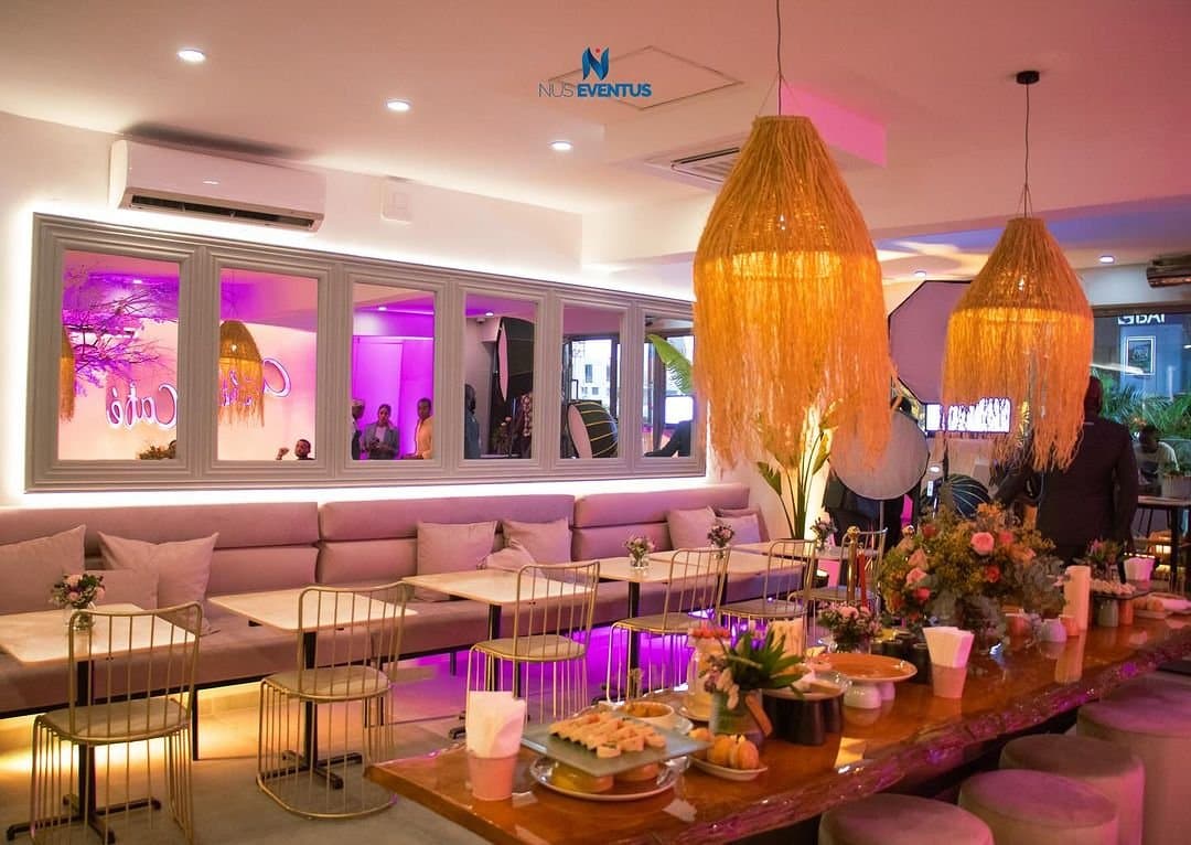 Lounge decorado com sofás, candeeiros de palha e luz rosa
